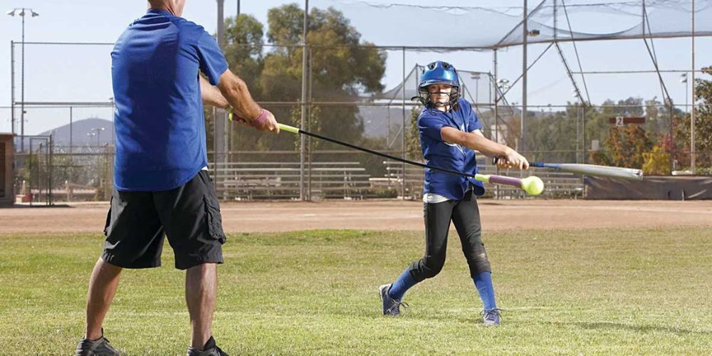 A man is teaching a young girl how to swing a baseball bat.