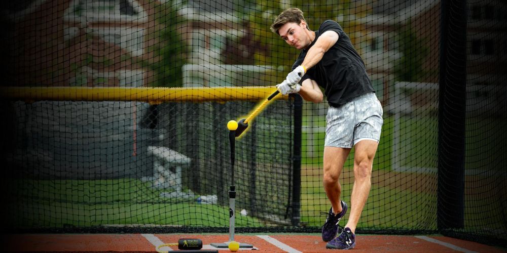 A man is swinging a bat at a baseball in a cage.