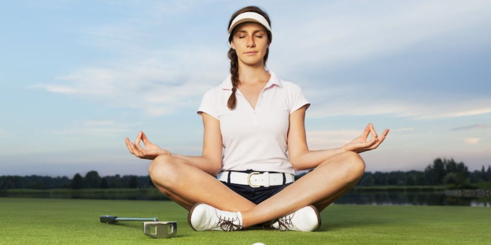 A woman is sitting in a lotus position on a golf course.