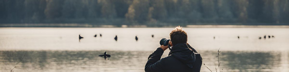 A man is taking a picture of a lake with a camera.