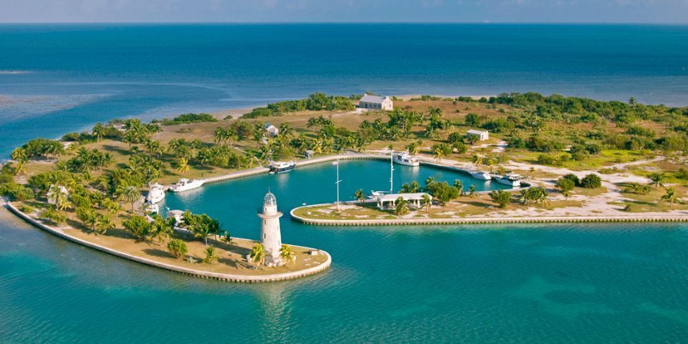 An aerial view of a small island with a lighthouse in the middle of the ocean.