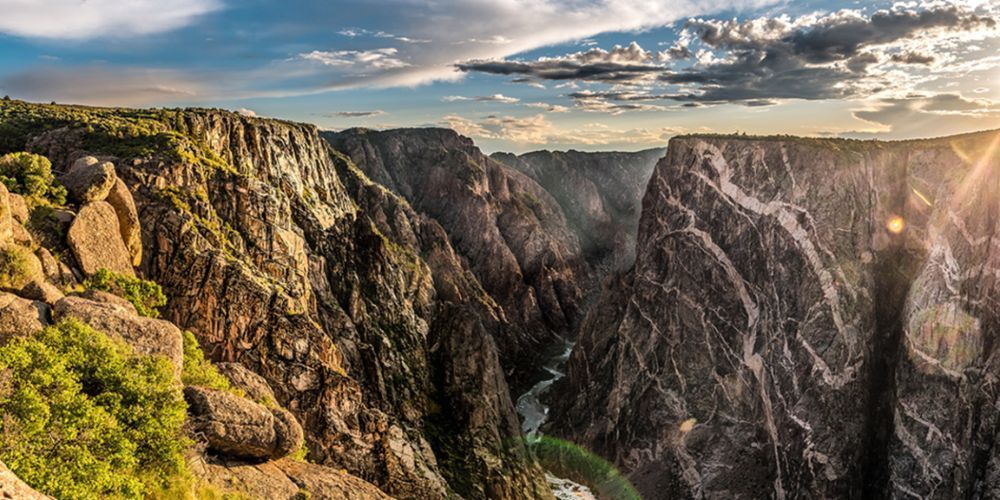 A canyon with a river running through it and the sun shining through the clouds.