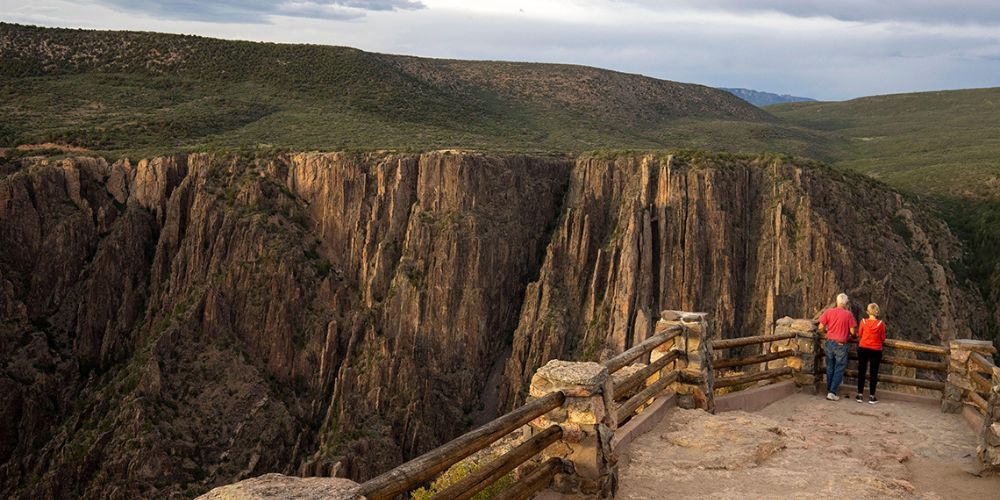 A couple standing on top of a cliff overlooking a canyon.