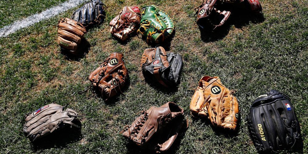 A bunch of baseball gloves are laying on the grass on a field.