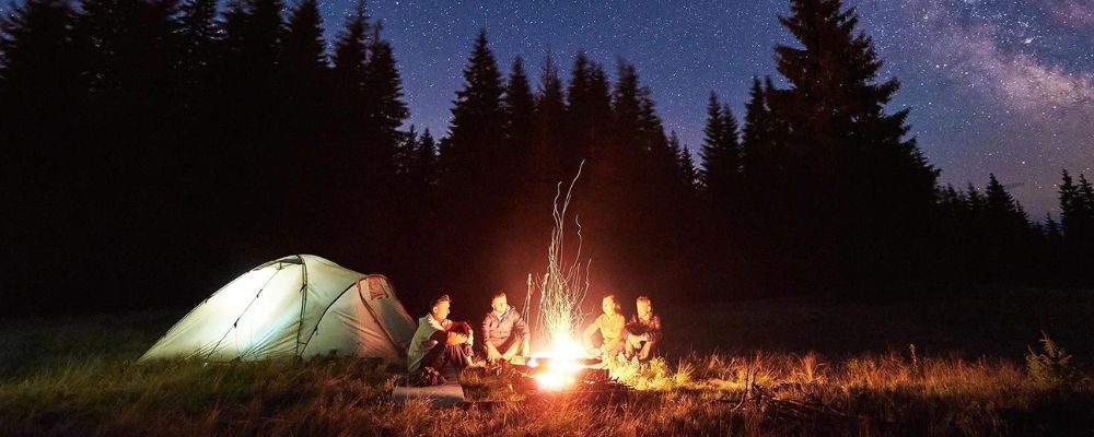 A group of people are sitting around a campfire in front of a tent at night.