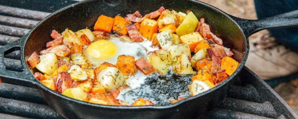 A skillet filled with eggs , potatoes , and bacon on a grill.