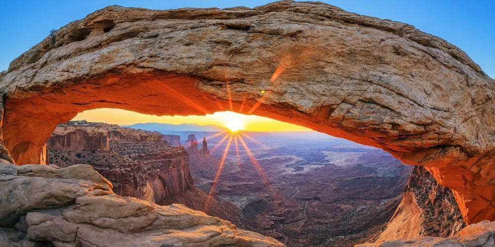 The sun is shining through a rock arch in the desert.