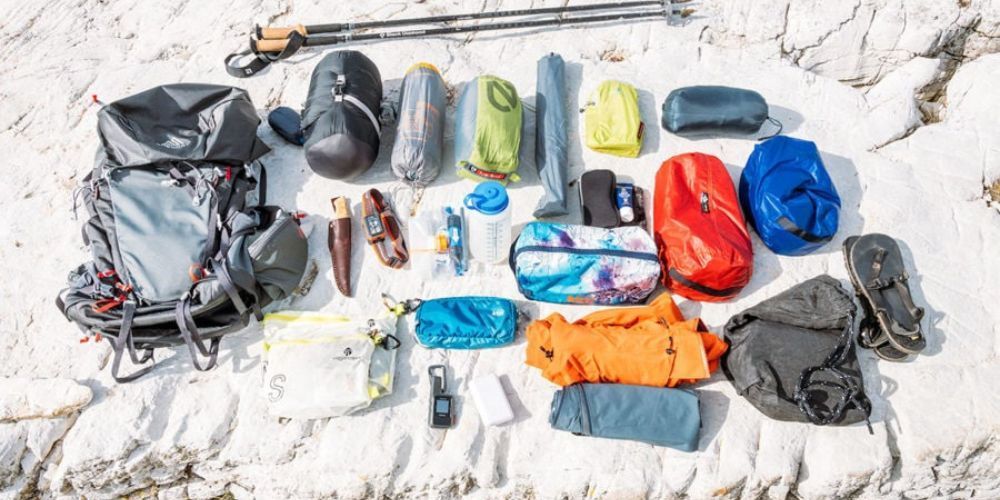 A bunch of hiking gear is laying on the sand.