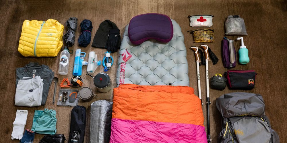 A sleeping bag is surrounded by a variety of camping equipment on a wooden floor.