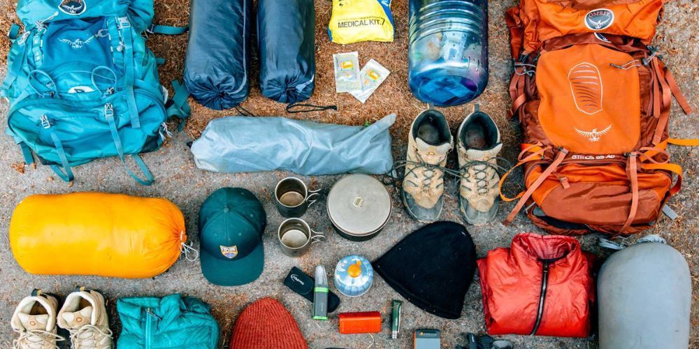 A bunch of backpacks , sleeping bags , shoes , hats , and other items are laid out on the ground.