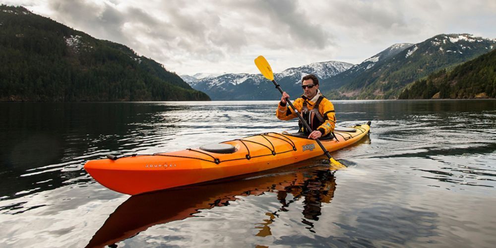 A man is paddling an orange kayak on a lake.