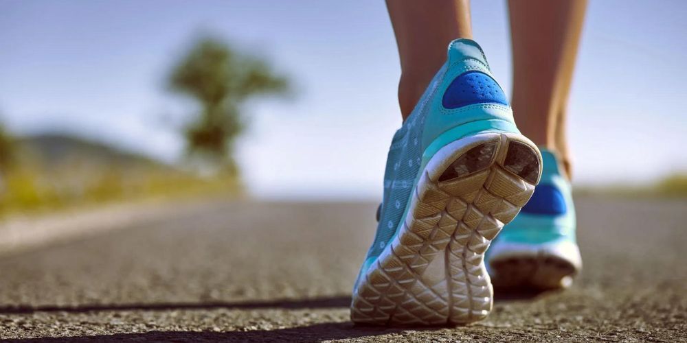 A woman is walking down a road wearing blue sneakers.