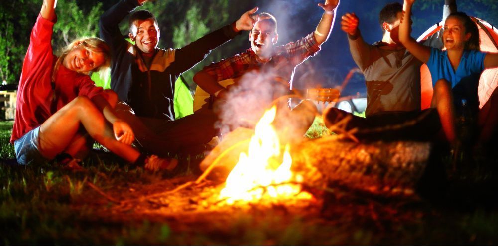 A group of people are sitting around a campfire at night.