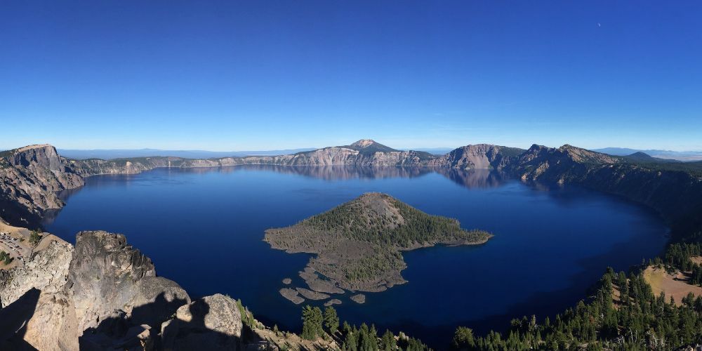 A large lake surrounded by mountains and trees with a small island in the middle.