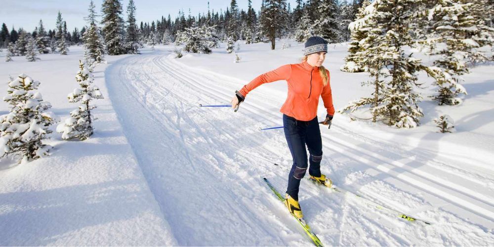 A woman is cross country skiing on a snowy trail.