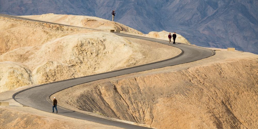 Two people are walking down a winding road in the desert.