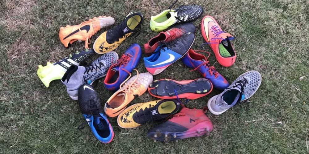 A bunch of soccer cleats are laying on the grass.