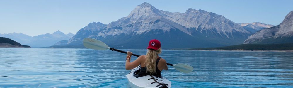 A woman is paddling a kayak on a lake with mountains in the background.