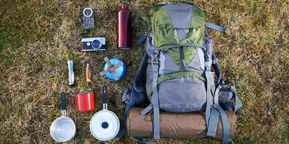 A backpack filled with camping supplies is laying on the grass.