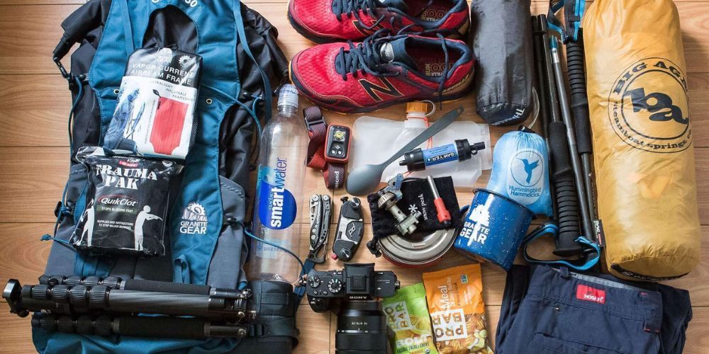 A backpack is filled with a lot of items , including shoes , a camera , and a tripod.