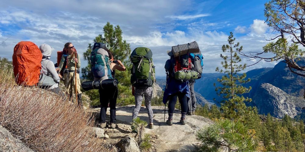 A group of people with backpacks are standing on top of a mountain.