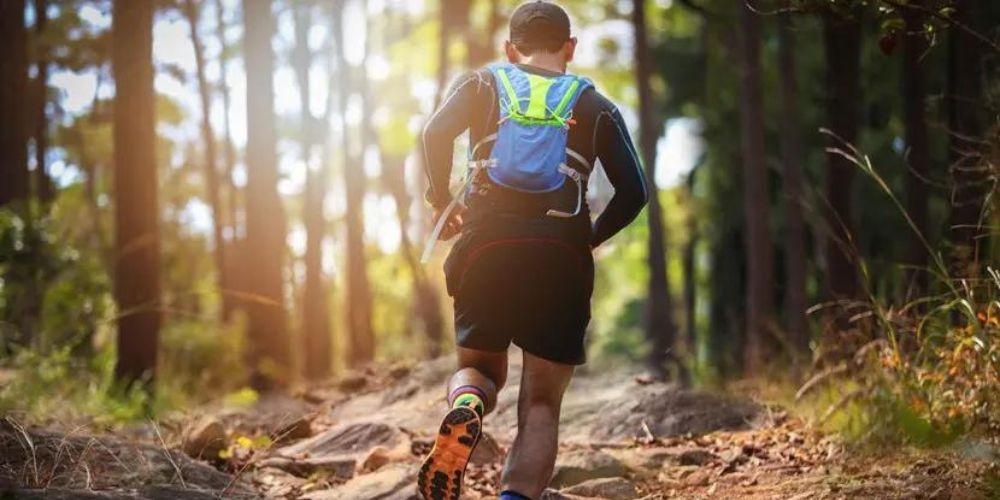 A man with a backpack is running on a trail in the woods.