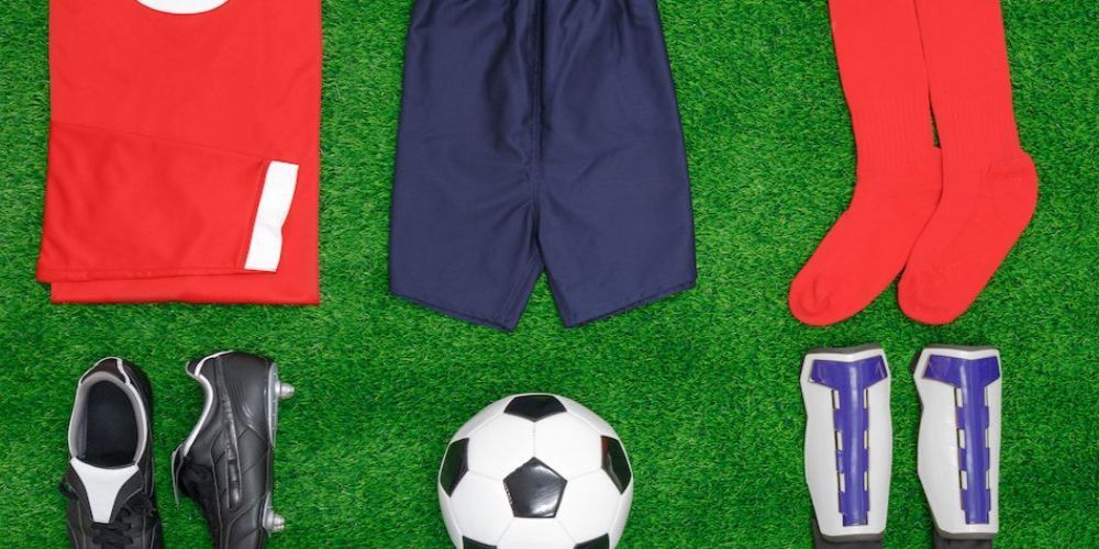 A soccer ball , soccer cleats , socks , shorts , and a jersey are on the grass.