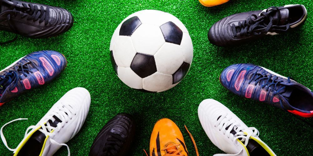 A soccer ball is surrounded by soccer cleats on a soccer field.