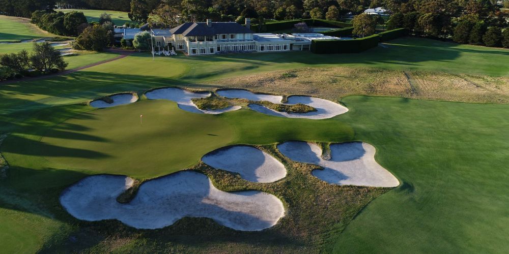 A golf course with bunkers and a house in the background.