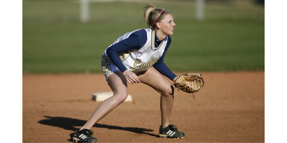 A woman is kneeling on a baseball field holding a glove.