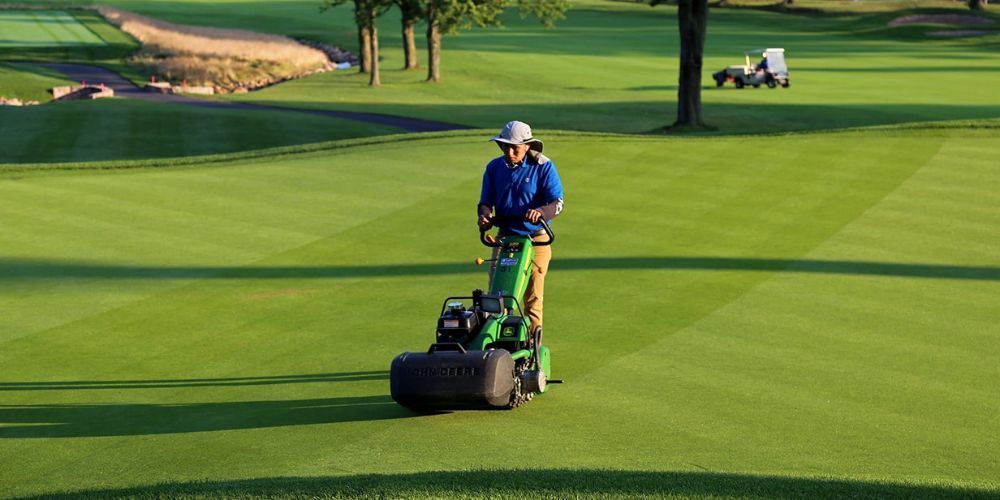 A man is riding a lawn mower on a golf course.