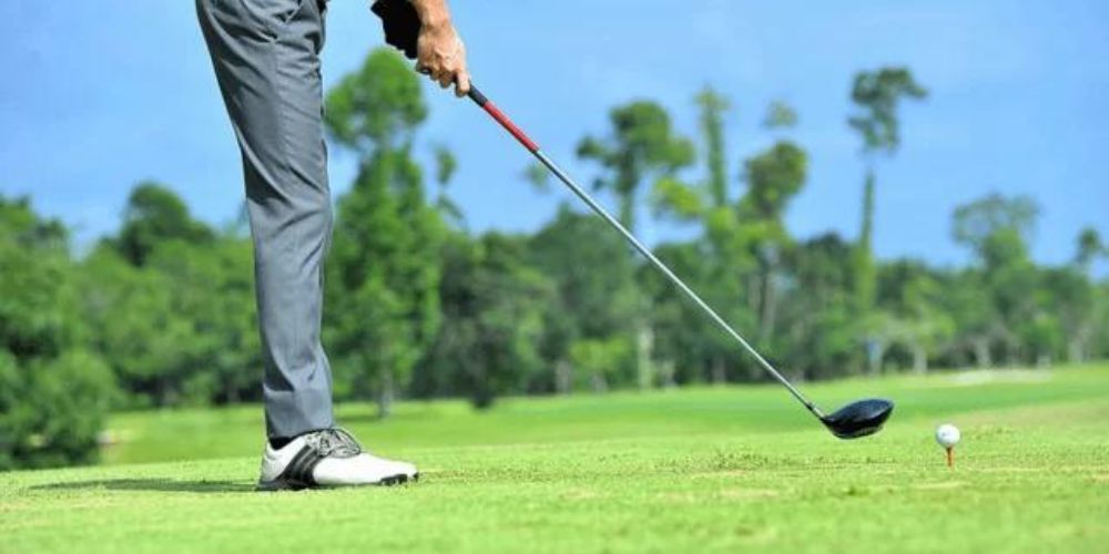 A man is swinging a golf club at a golf ball on a golf course.