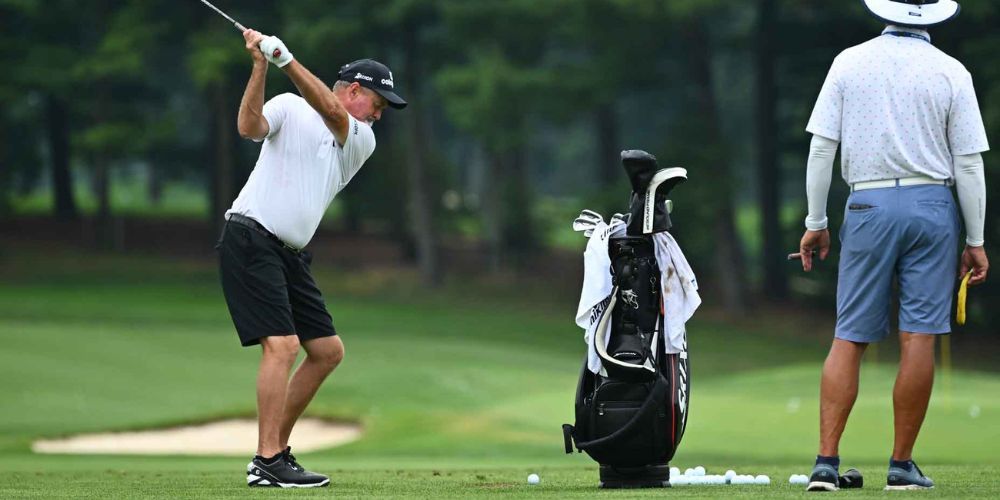 A man is swinging a golf club on a golf course while another man watches.