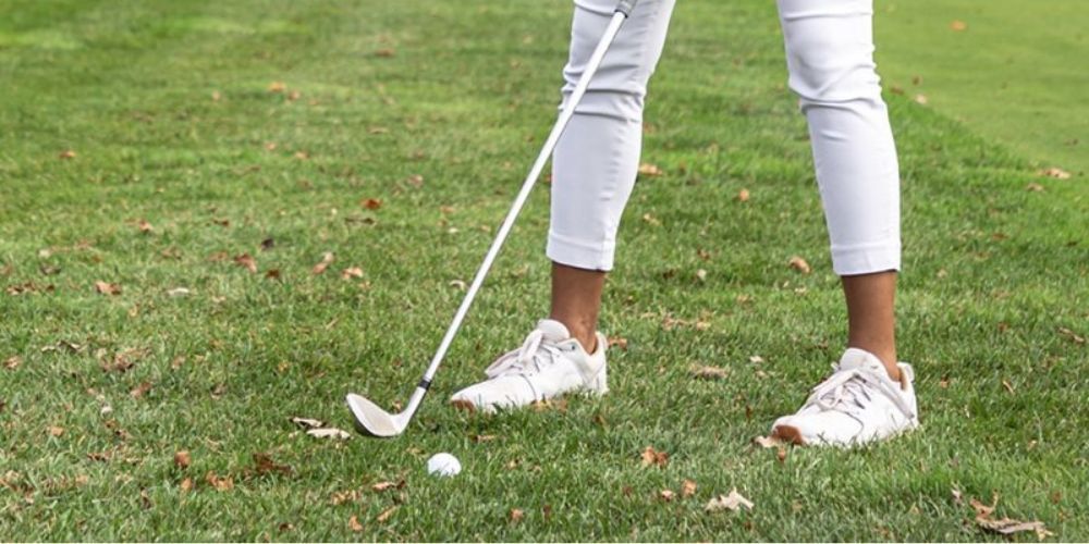 A woman is swinging a golf club at a golf ball on a golf course.