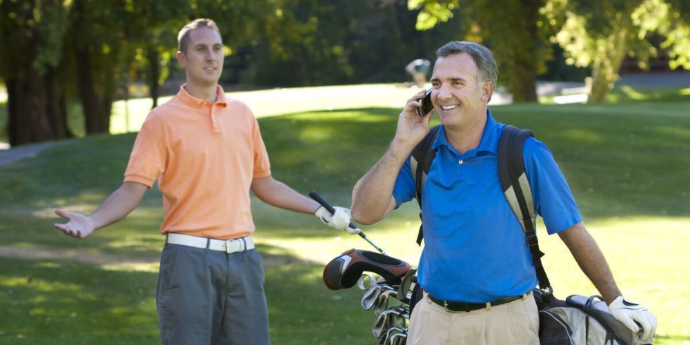 Two men are playing golf and one is talking on a cell phone