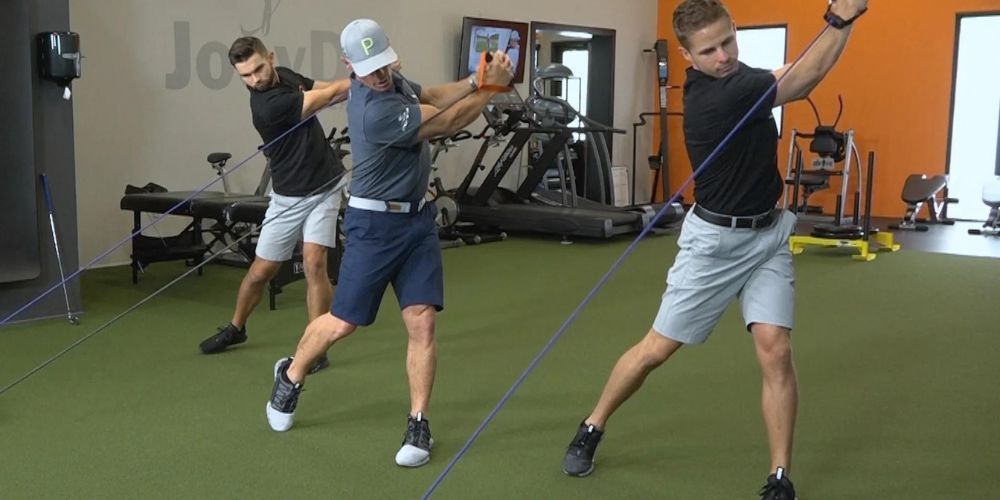 Three men are doing exercises in a gym with a rope.