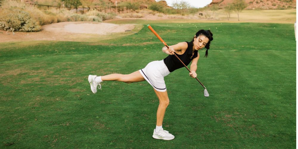 A woman is swinging a golf club on a golf course.