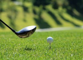 A golf club is hitting a golf ball on a tee.