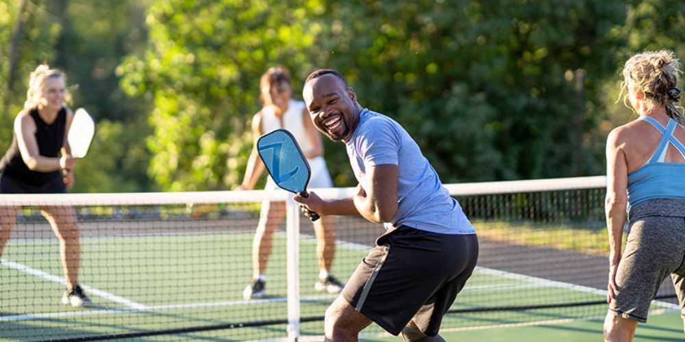 A group of people are playing pickleball on a tennis court.