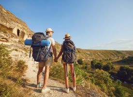 A man and a woman with backpacks are holding hands while hiking up a hill.