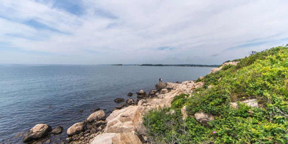 A rocky cliff overlooking the ocean on a cloudy day.