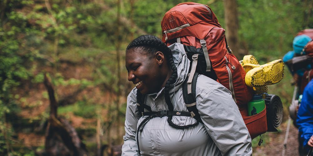 A woman with a backpack is walking through the woods.