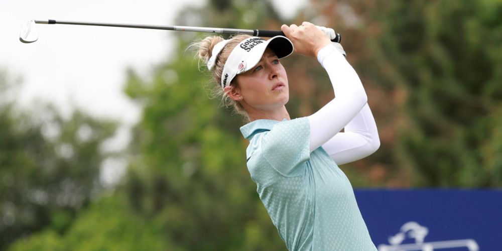 A woman is swinging a golf club on a golf course.