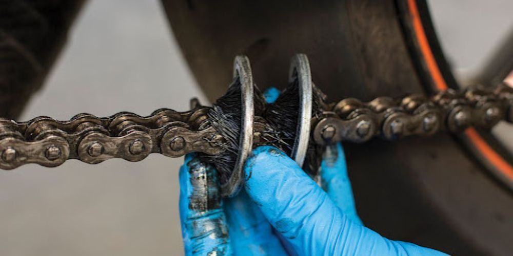 A person wearing blue gloves is cleaning a motorcycle chain.