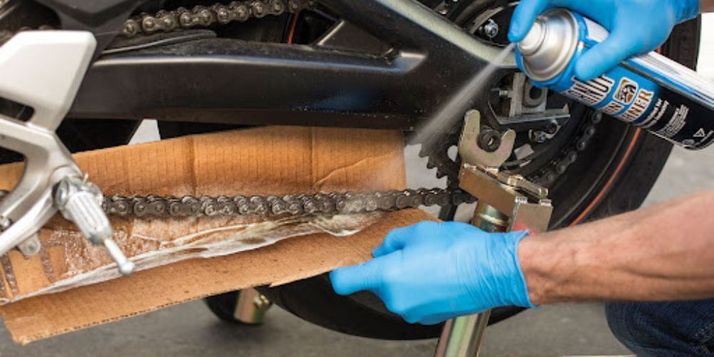 A person is spraying a motorcycle chain with a spray can.