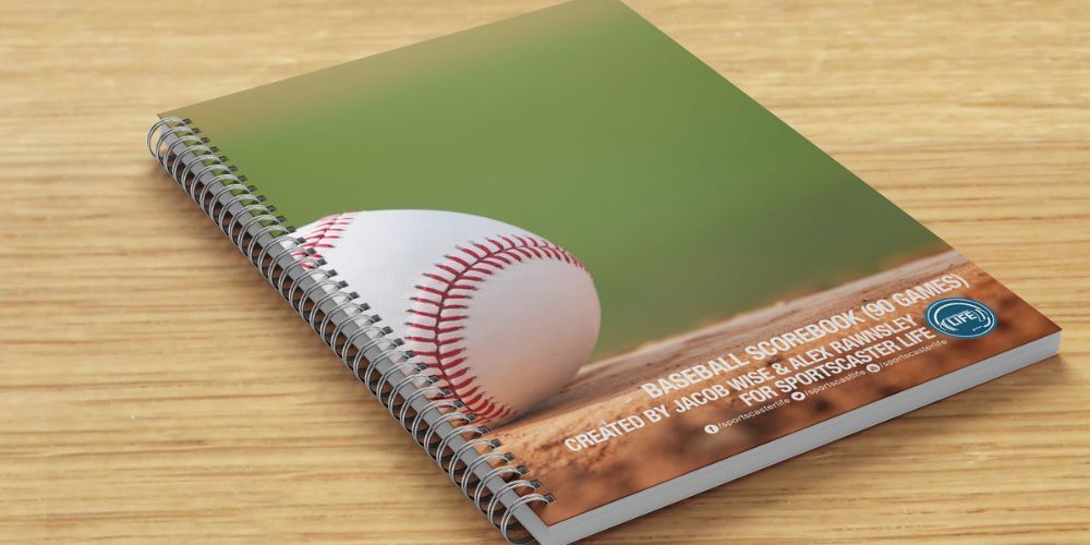 A spiral notebook with a baseball on the cover is sitting on a wooden table.