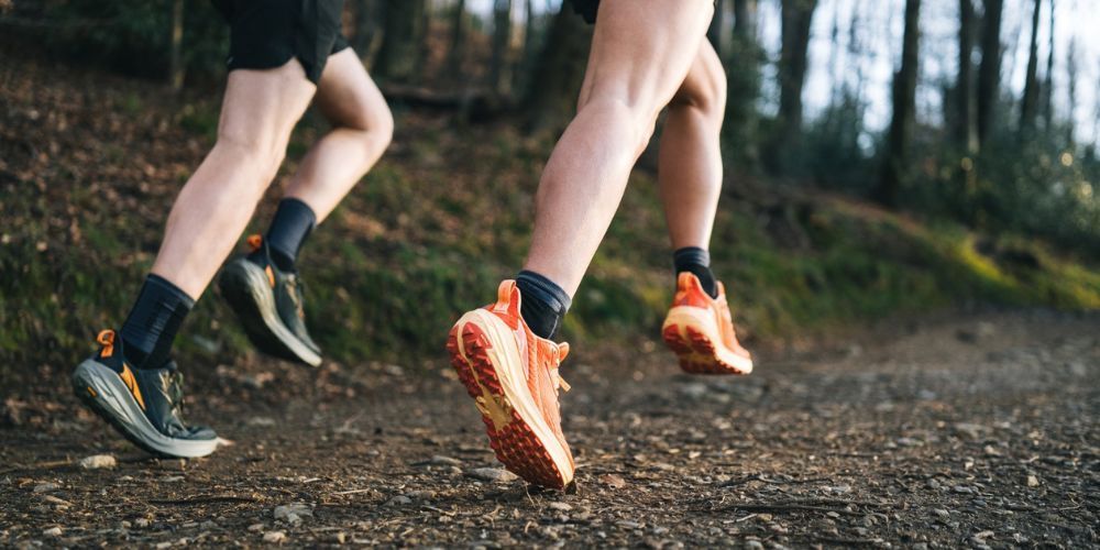 A couple of people are running on a trail in the woods.