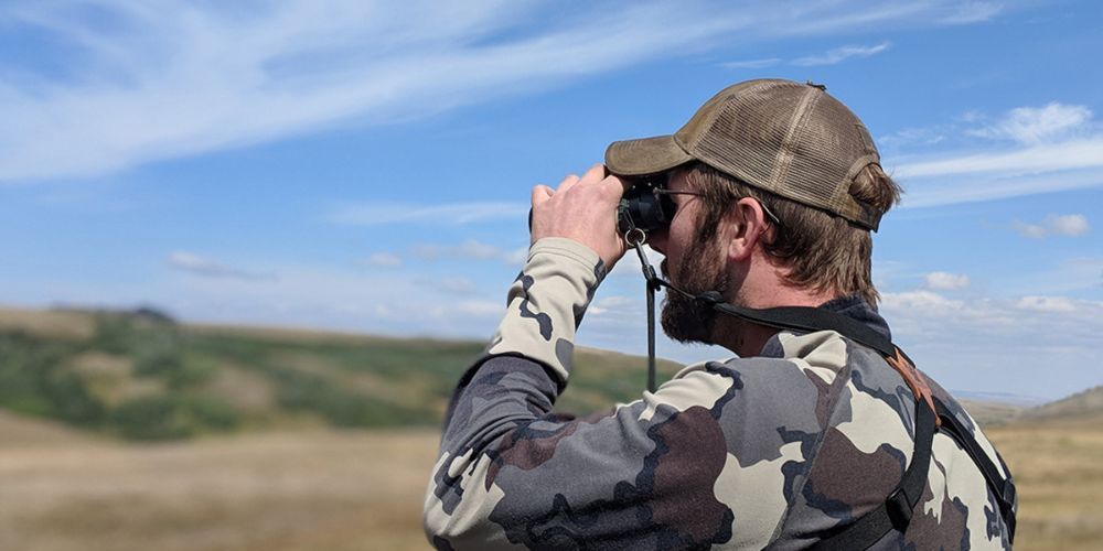 A man is looking through binoculars in a field.