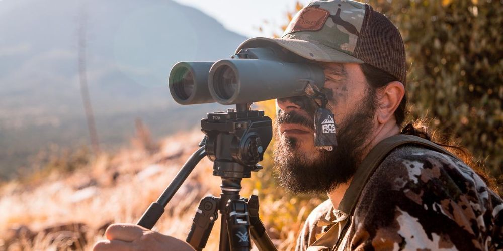 A man is looking through binoculars on a tripod.