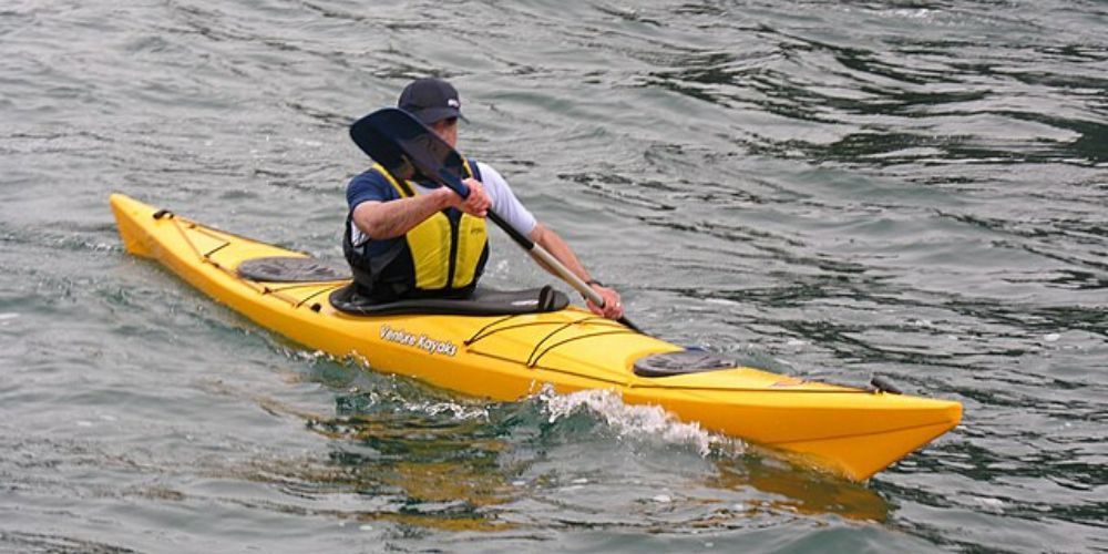 A man is paddling a yellow kayak in the water.